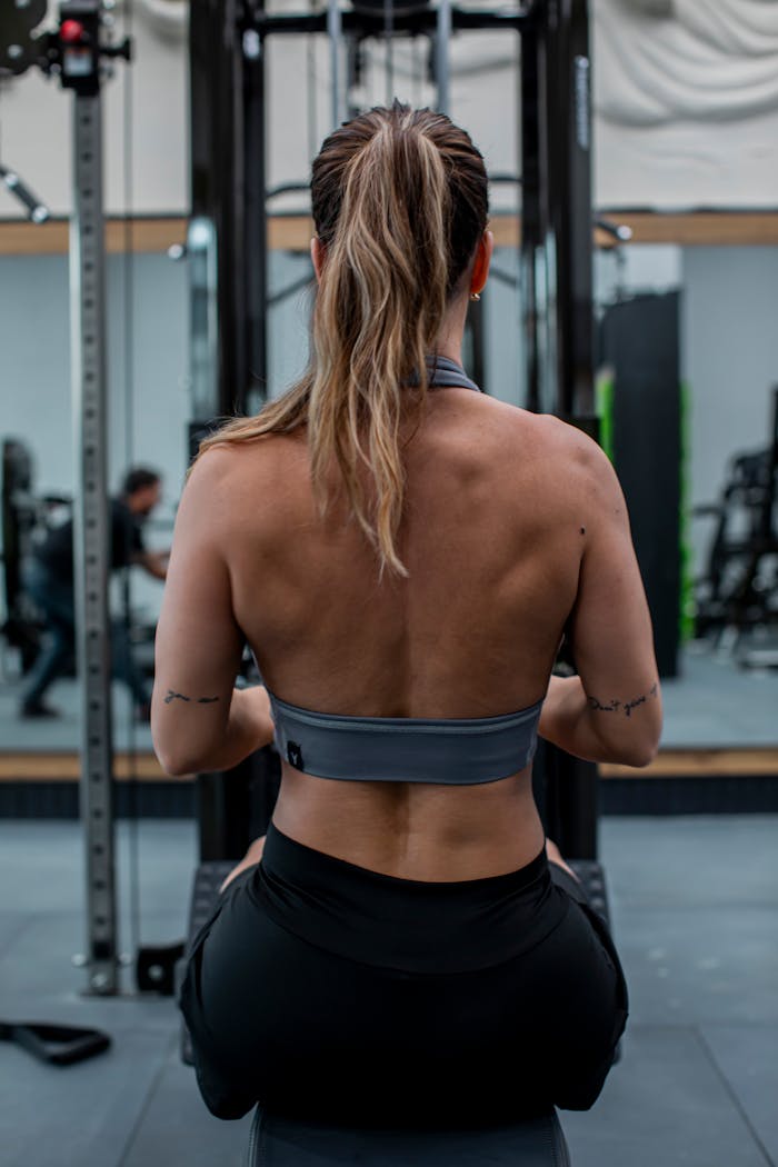 About Back view of a female athlete exercising in a gym, focusing on her workout routine.